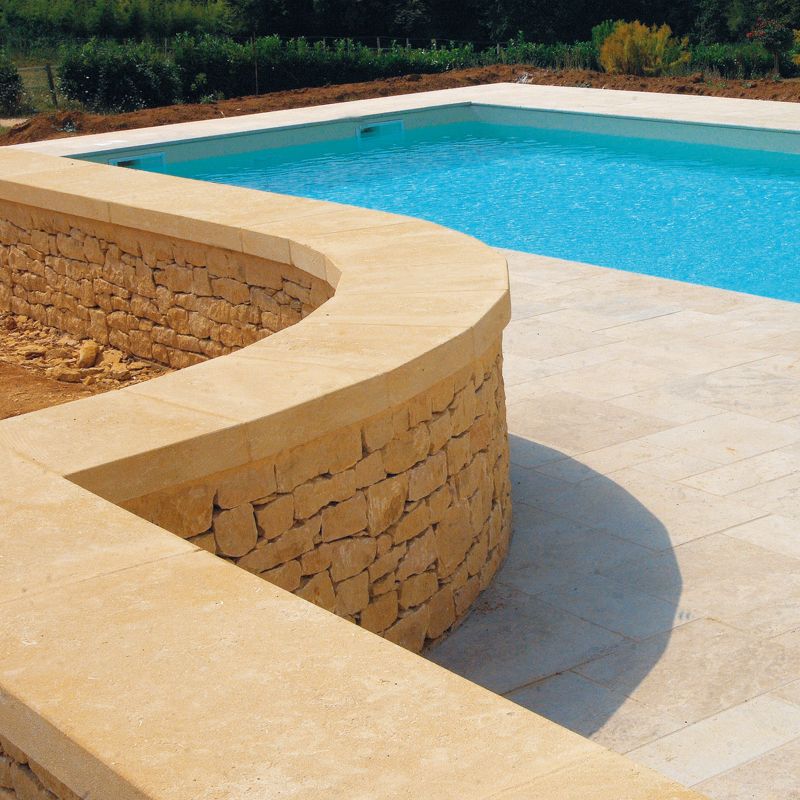 Dessus de mur en pierre naturelle beige avec parement en pierre sèche, entourant une piscine pour un aménagement extérieur élégant.