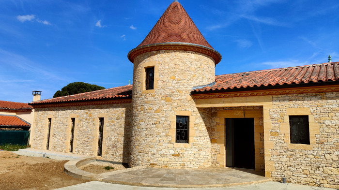 Maison avec façade en pierre naturelle et tour ronde, réalisée en pierre calcaire taillée, alliant authenticité et élégance architecturale.